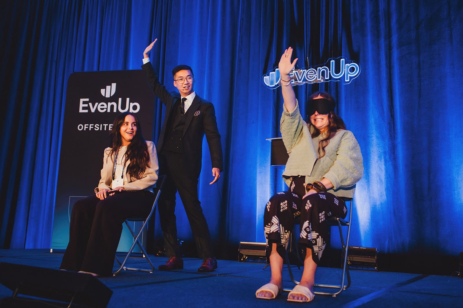 Two blindfolded EvenUp guests seated on stage raising their hands while Bao stands between them