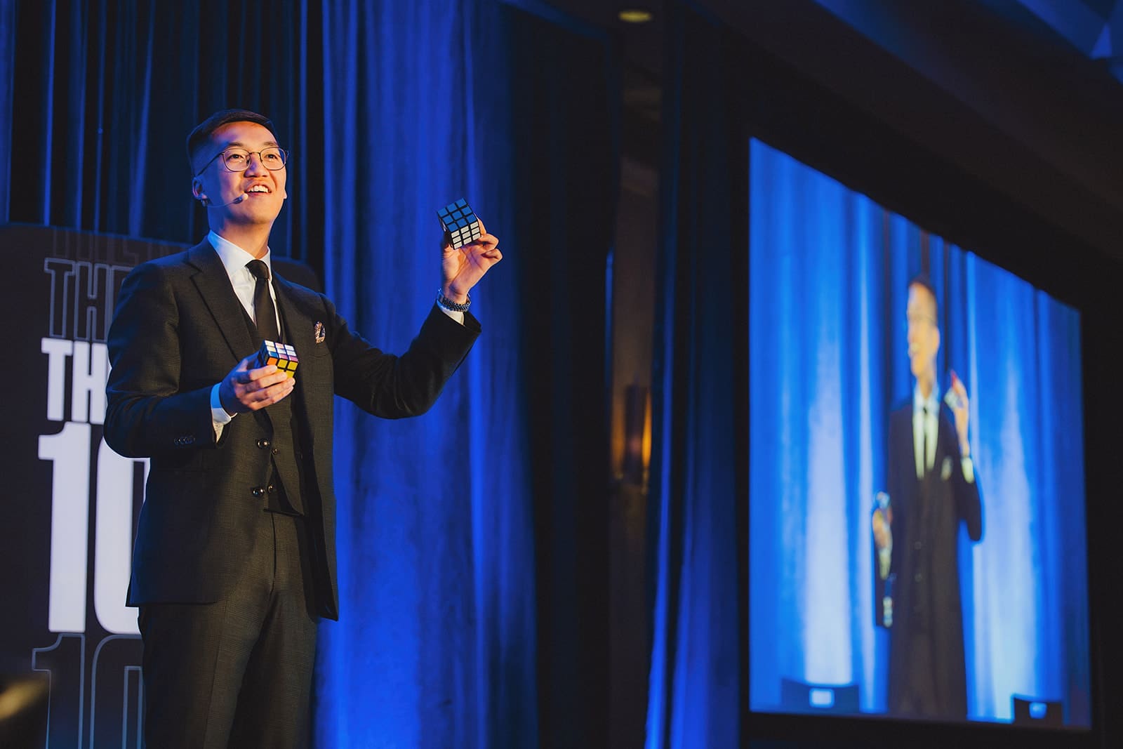 Bao on stage at the EvenUp offsite with the live camera feed showing him on the projection screen beside the stage
